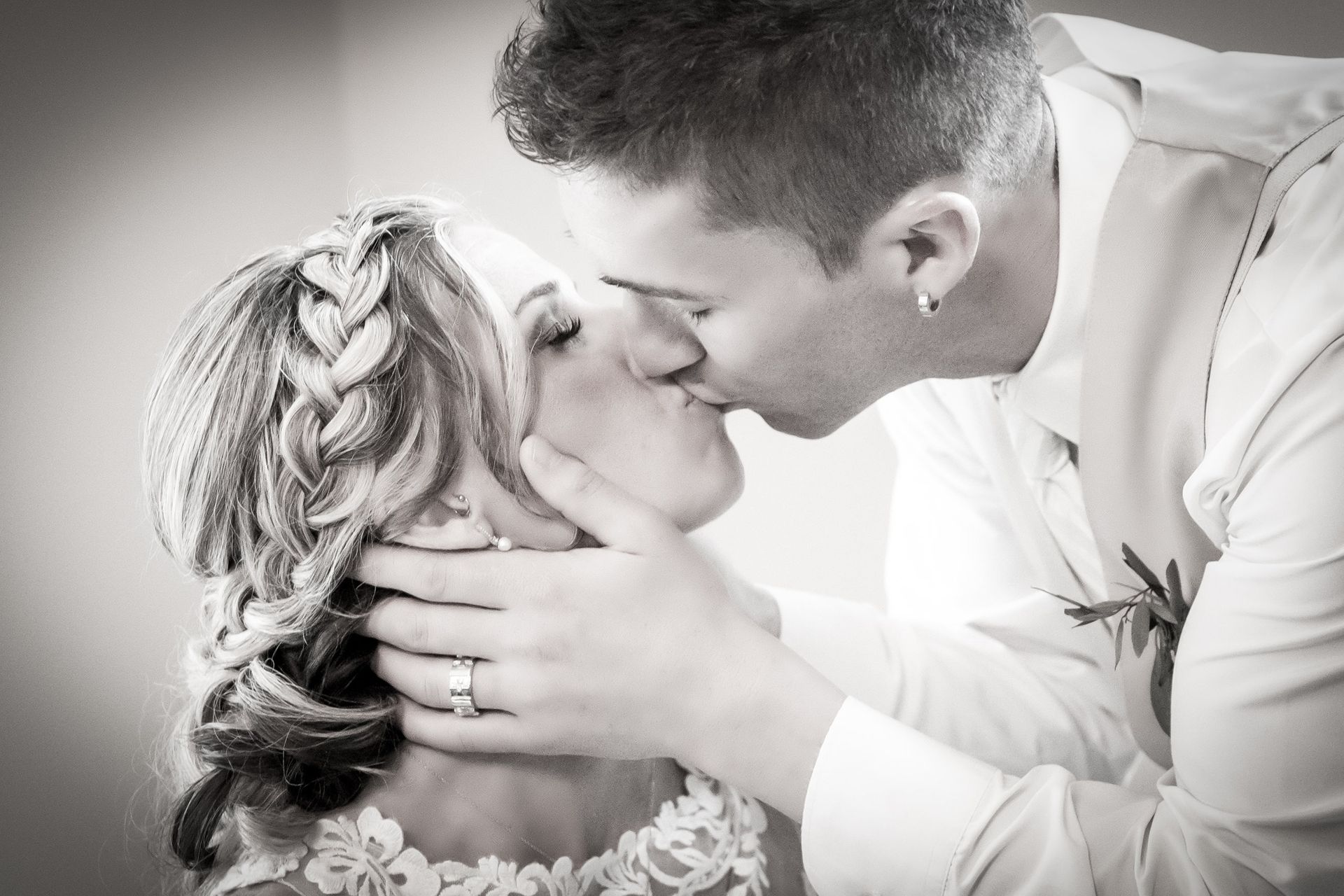Bride and groom kissing; her hair in braid, he has earring, both in formal attire.