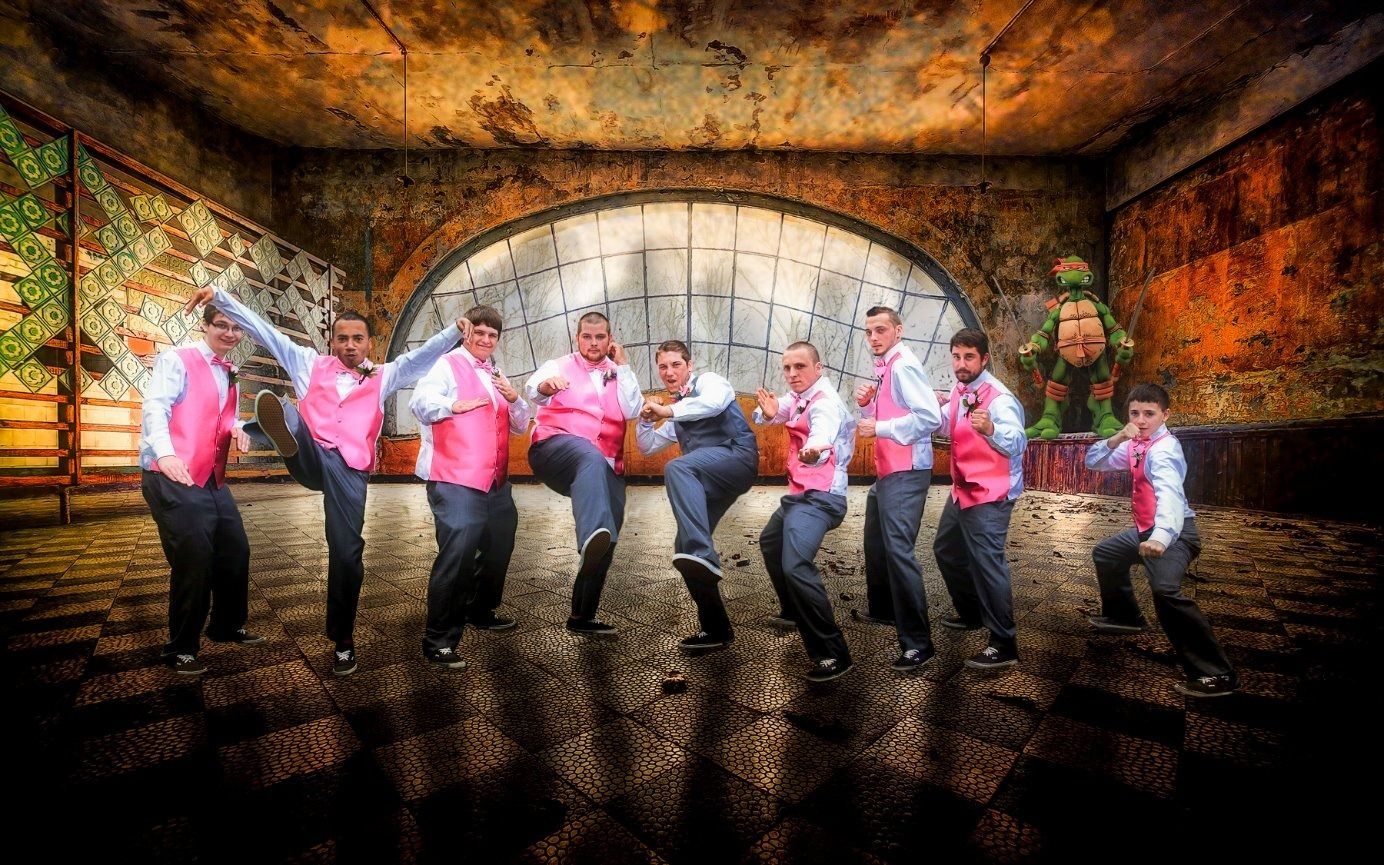 Group of men in pink vests and dress pants strike action poses in a grungy, old building.