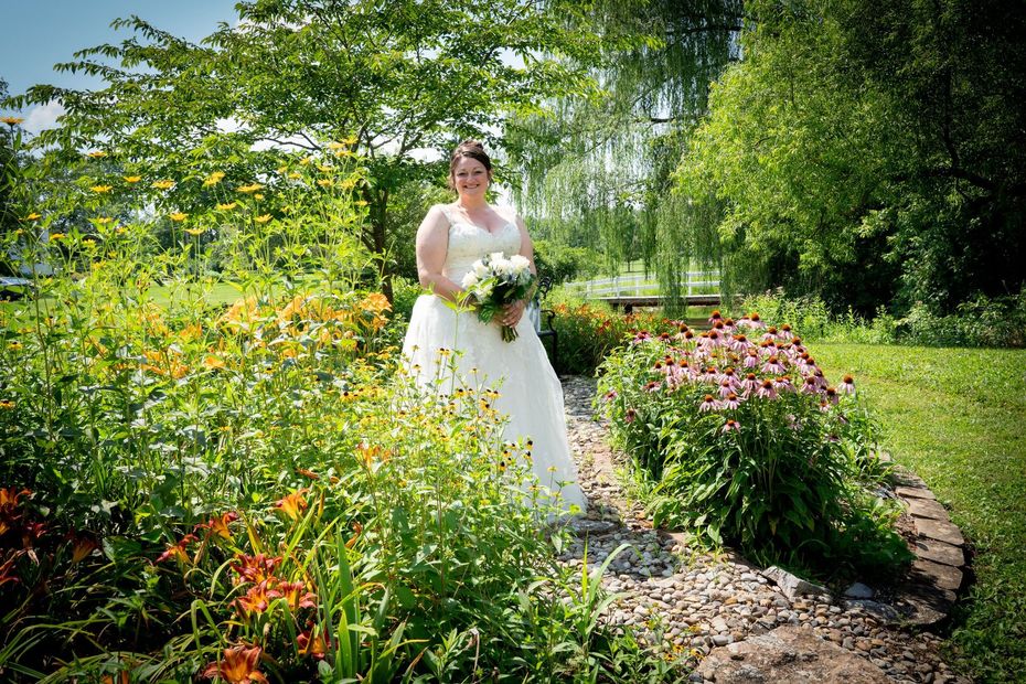 Bride in a white gown holding flowers, smiles in a colorful garden during daytime.