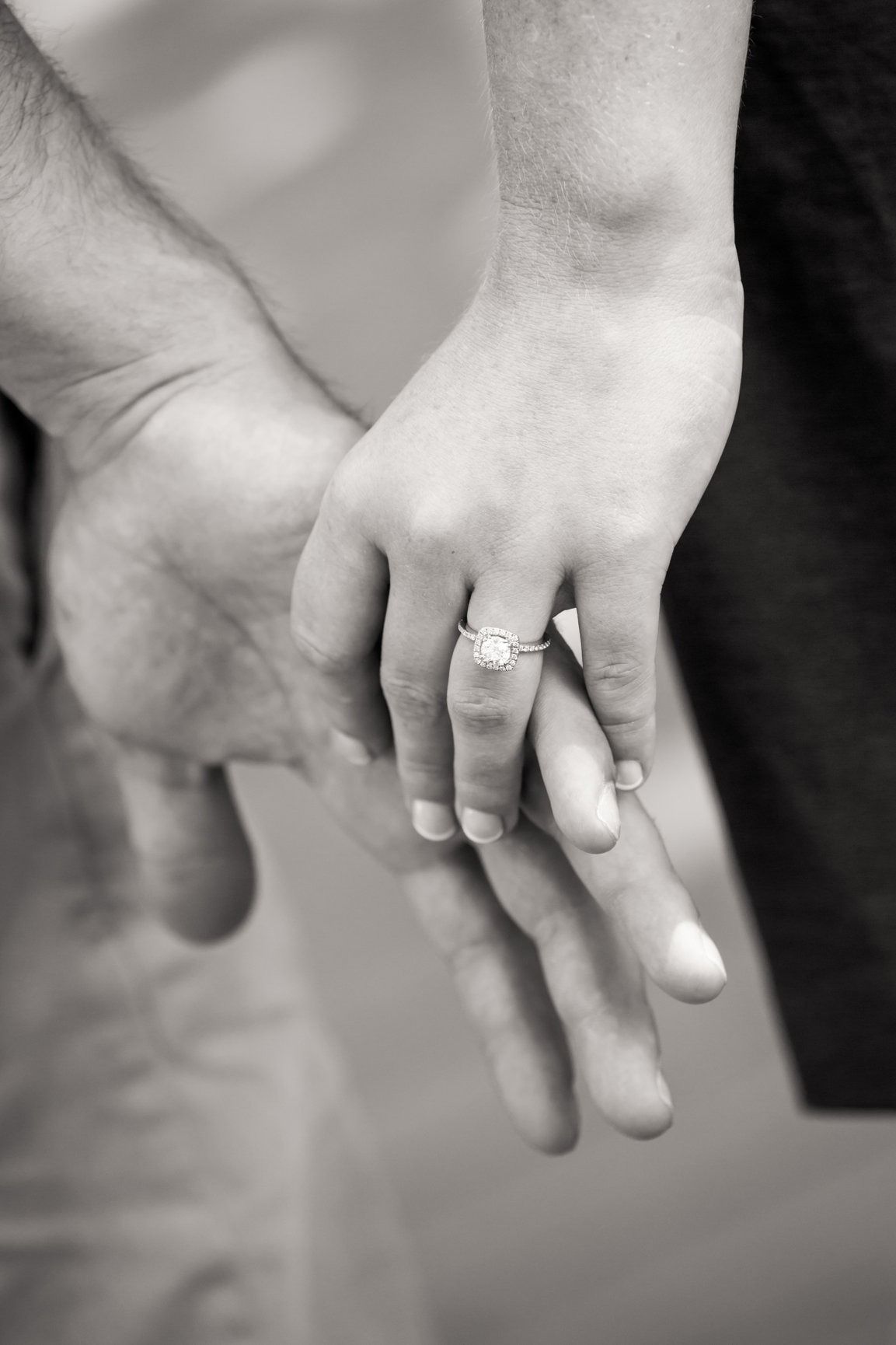 Hands clasped, woman's ringed finger resting on man's palm, symbolizing engagement.