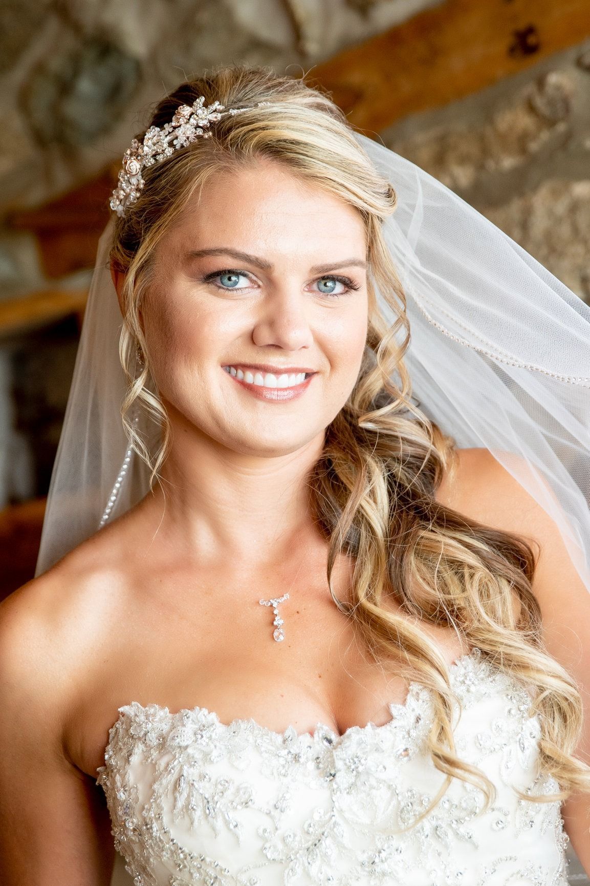 Bride in a strapless white dress smiling, wearing a veil and headpiece.