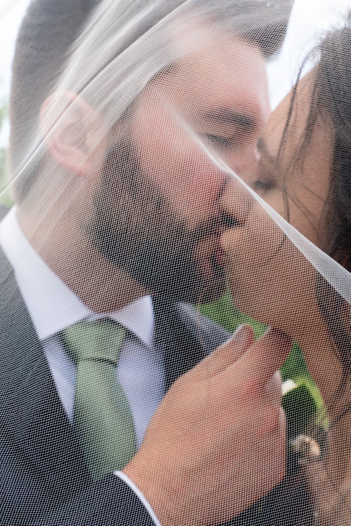 Man kissing a person through a sheer veil; he wears a suit and green tie.