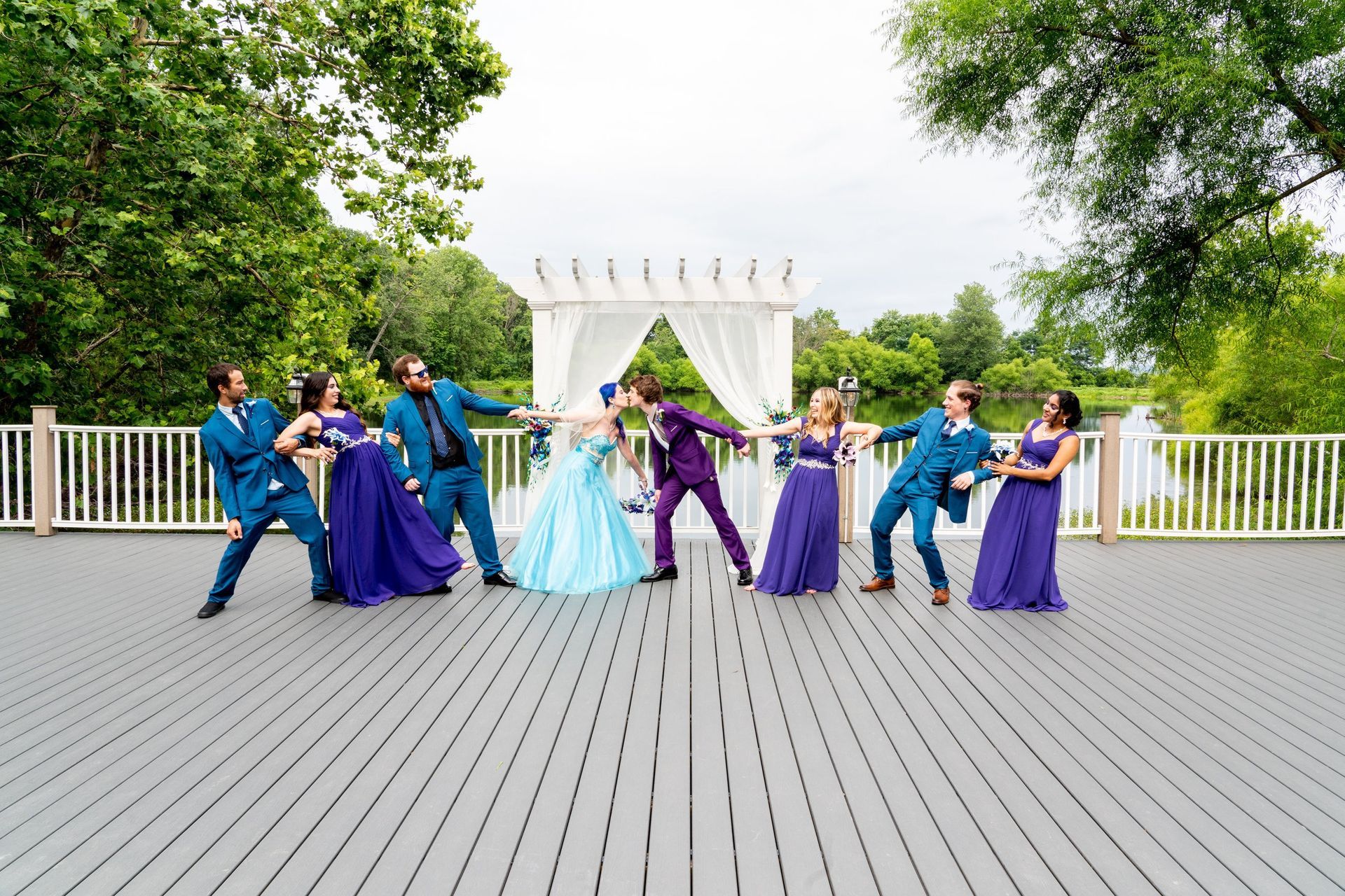 Wedding party on deck: couple kissing, attendants striking playful poses, teal/purple attire.