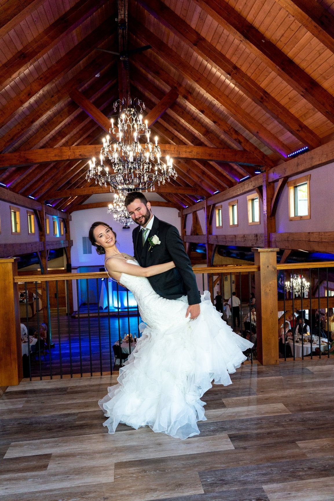 Bride and groom dancing at their wedding in a rustic barn with chandelier, wooden beams.