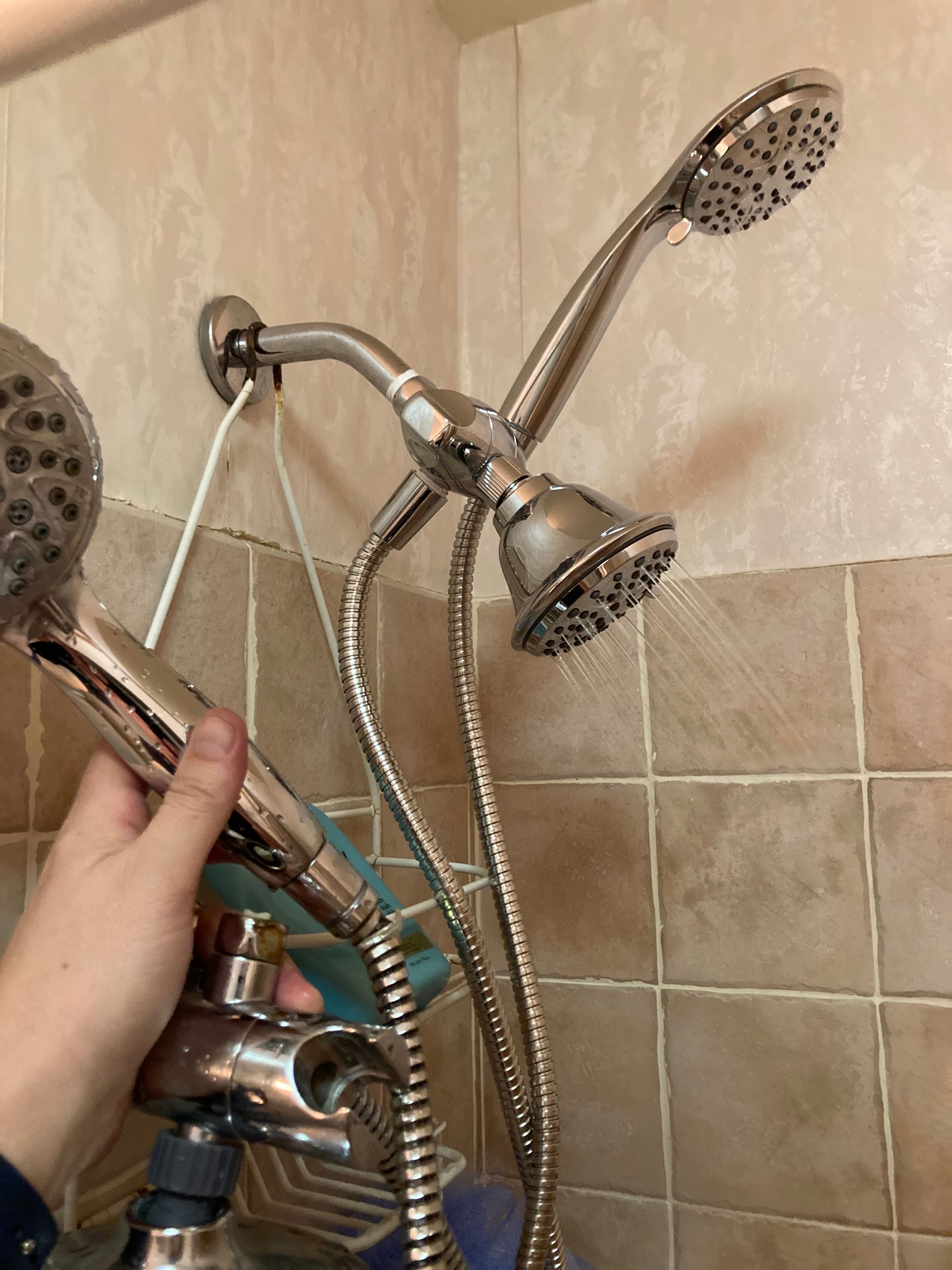 A person is holding a shower head in their hand in a bathroom.