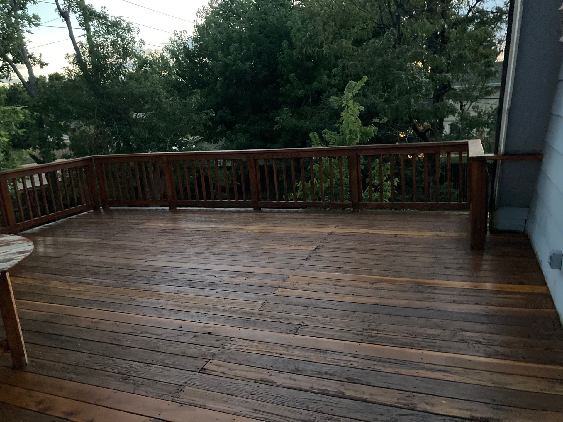 A large wooden deck with a railing and trees in the background.