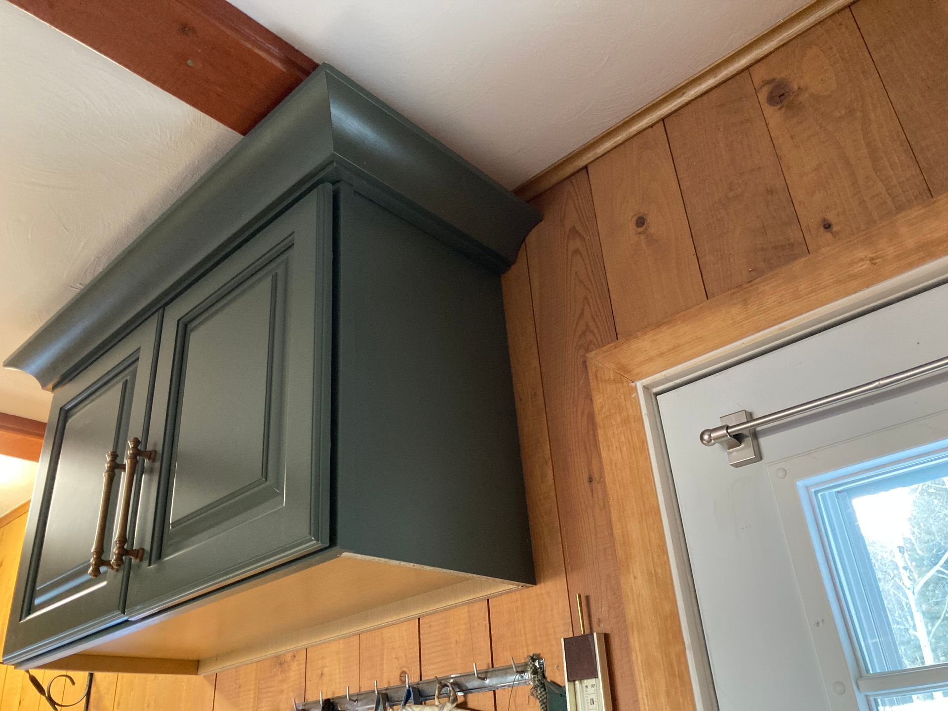 A green cabinet is hanging from the ceiling above a door.