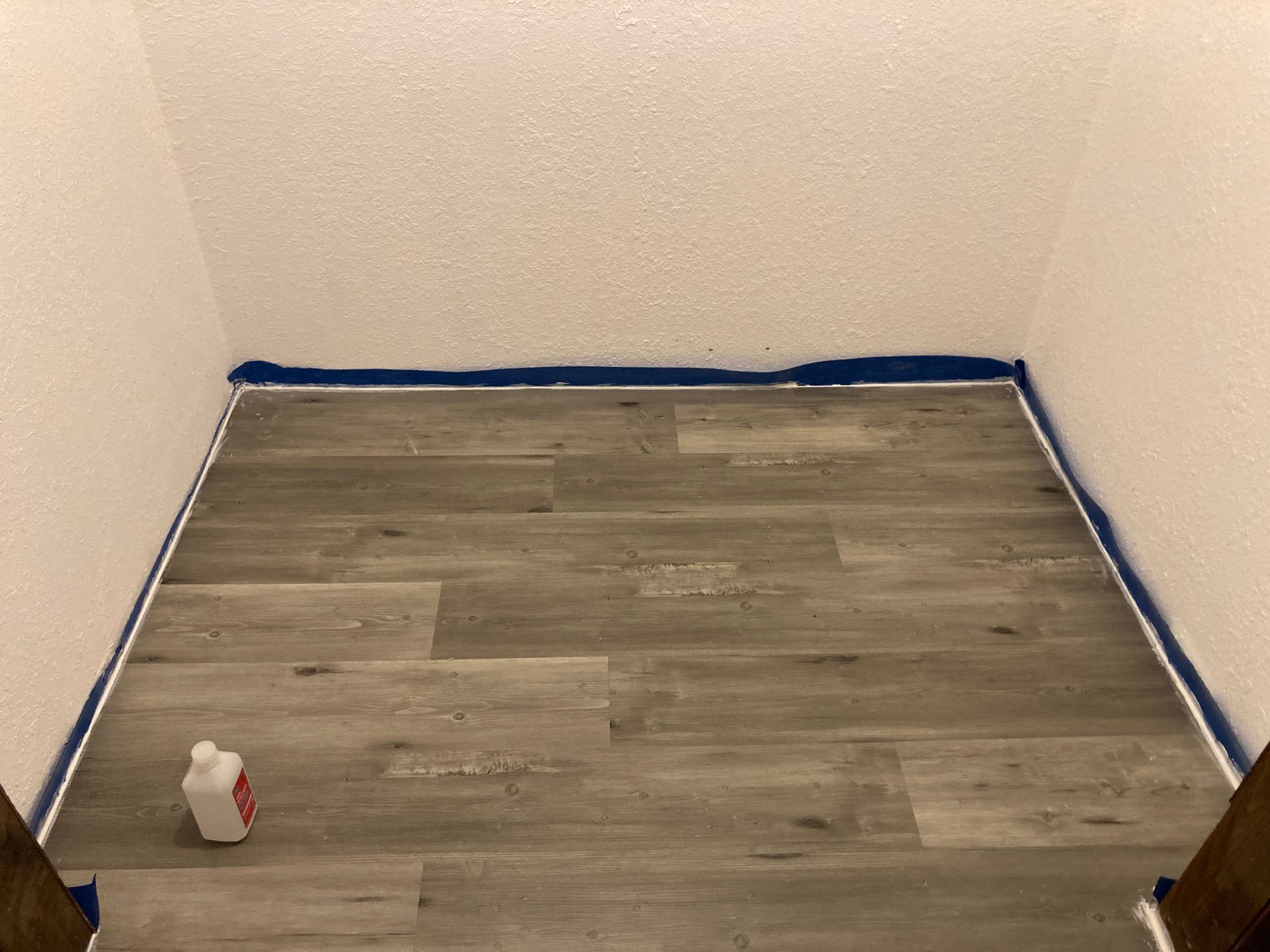 A room with a wooden floor and a bottle of cleaner on the floor.