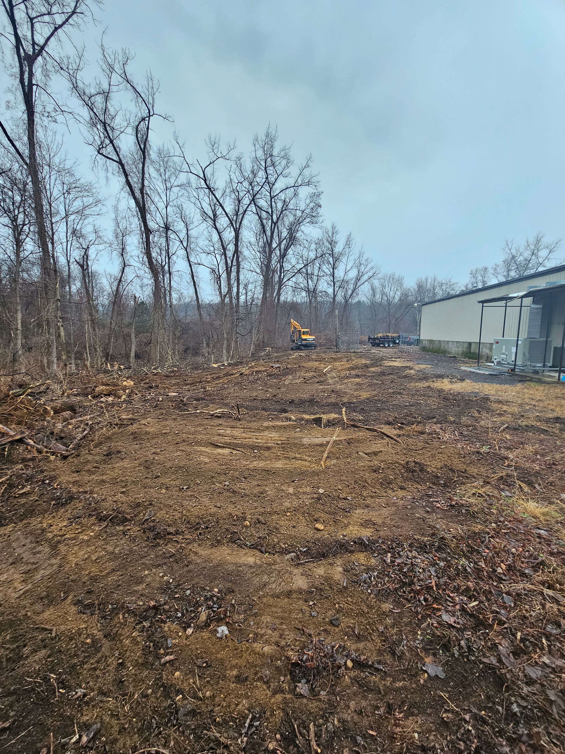 A large dirt field with trees in the background and a building in the background.