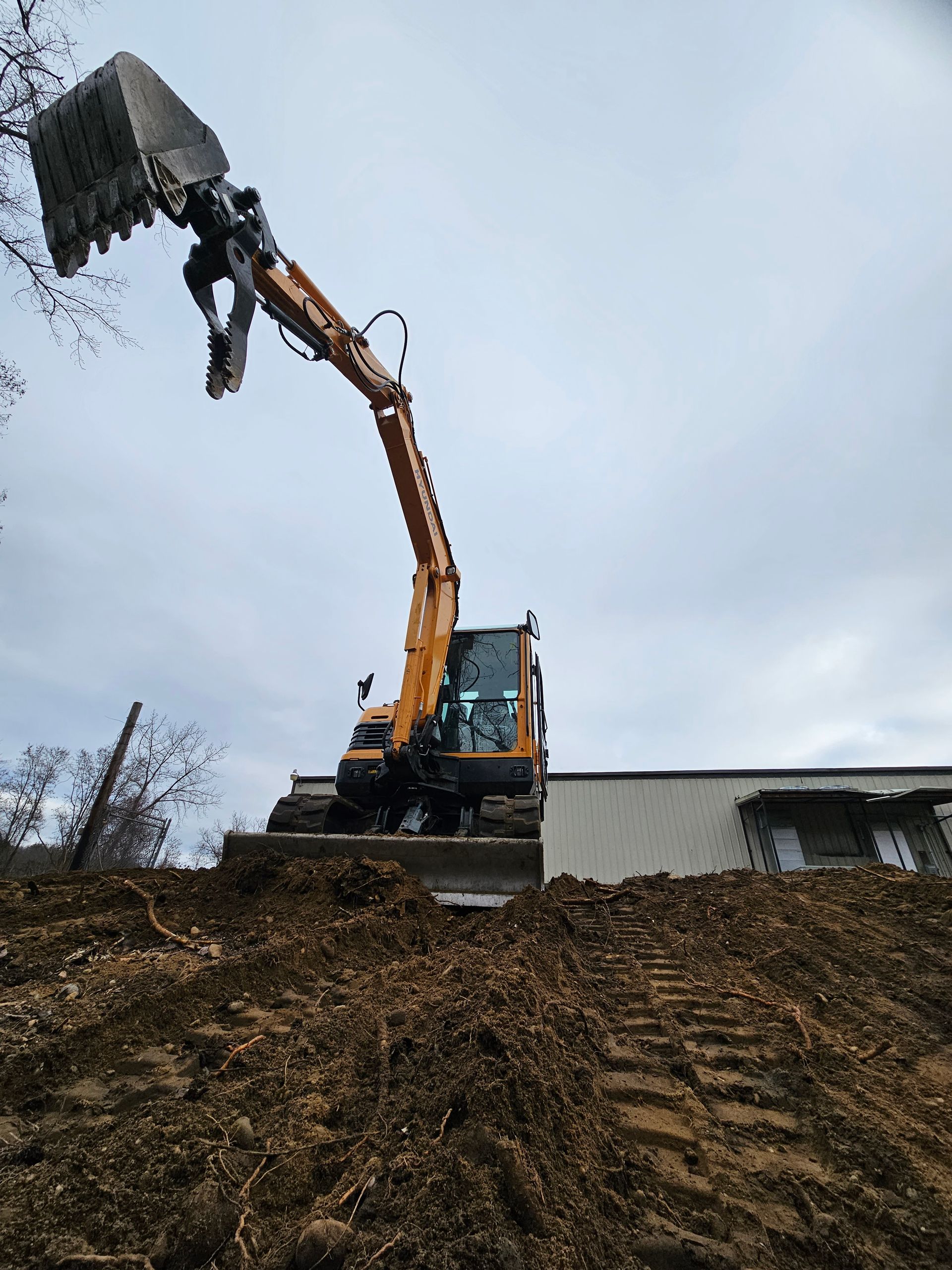 An excavator is digging a hole in the dirt in front of a building.