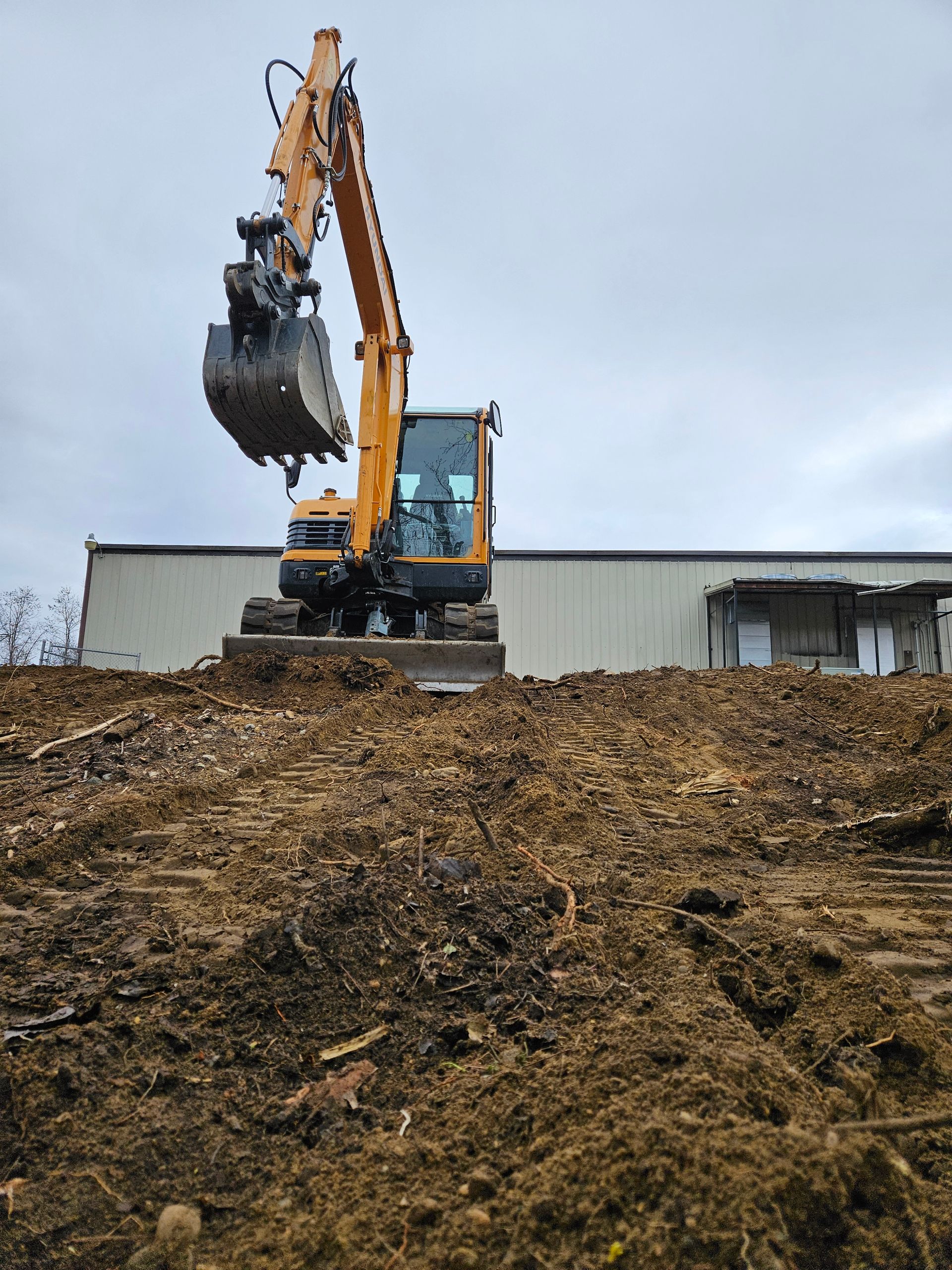 A yellow excavator is digging a pile of dirt in front of a building.