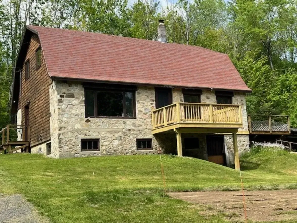 A large stone house with a red roof and a wooden deck.