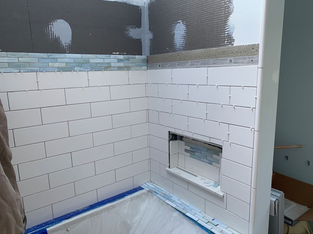 A bathroom being remodeled with white tiles and a blue tape on the floor.