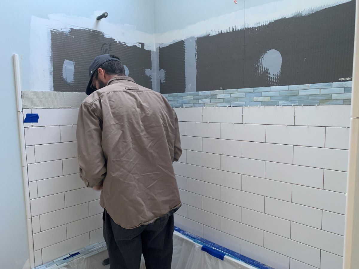 A man is installing tiles on a bathroom wall.