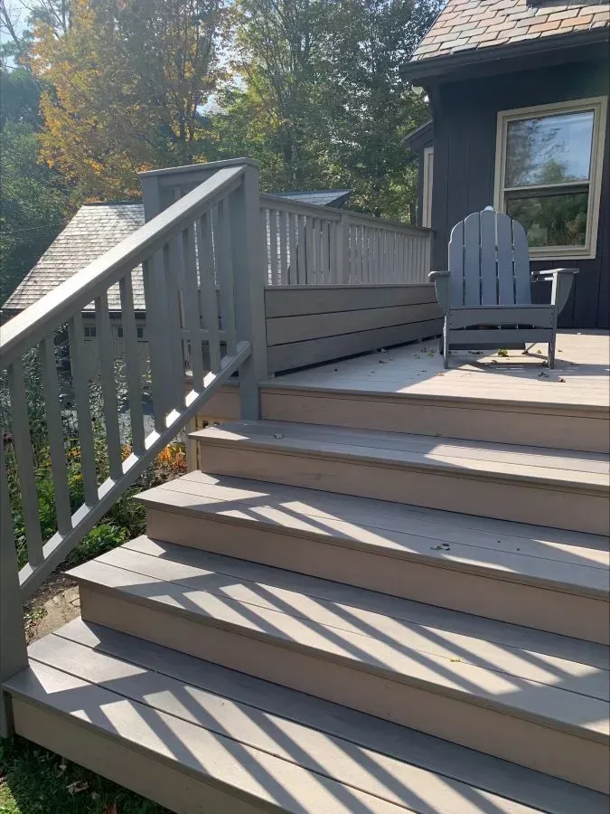 A deck with stairs and a chair on it in front of a house.