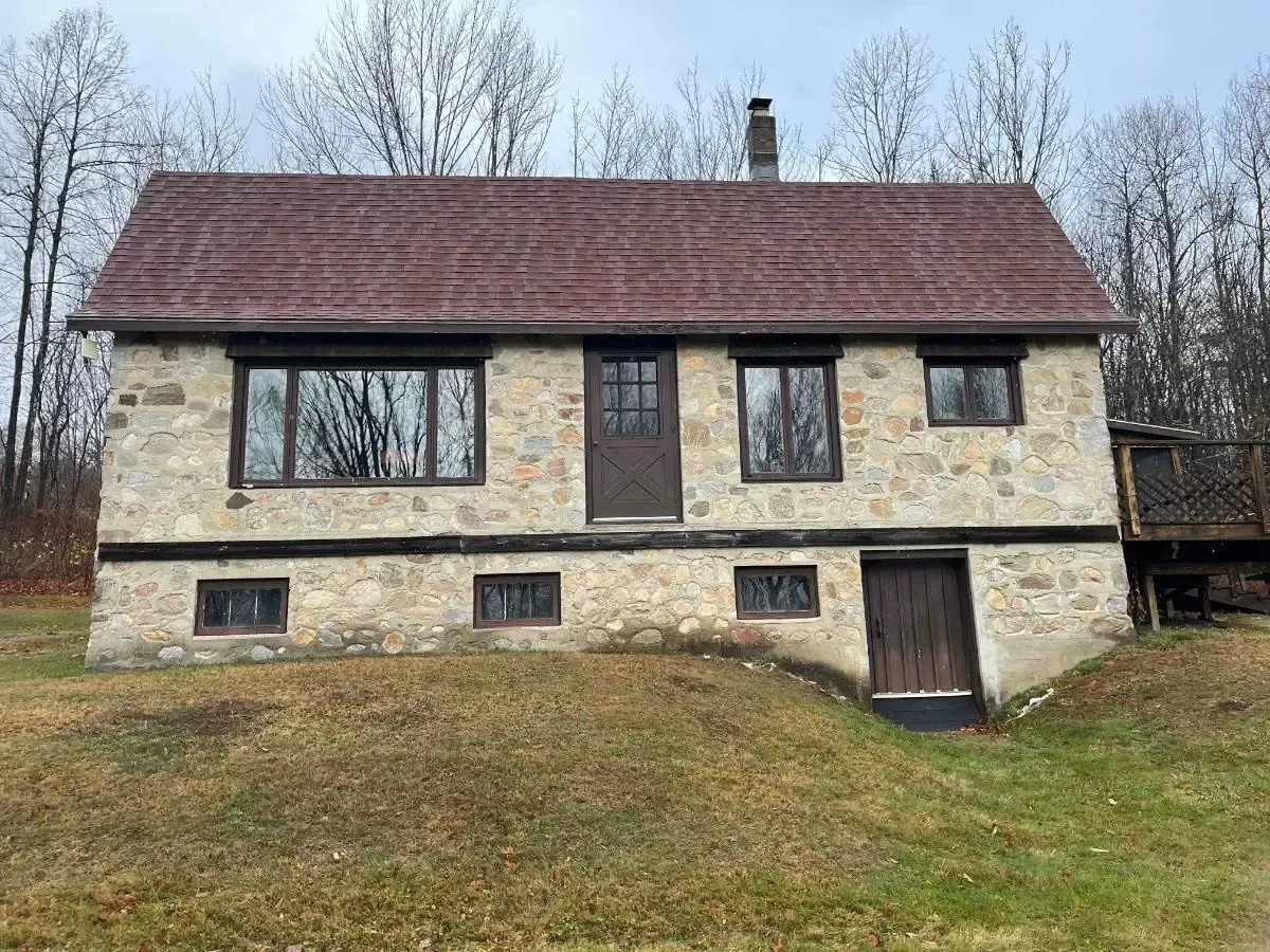 A large stone house with a red roof is sitting on top of a grassy hill.