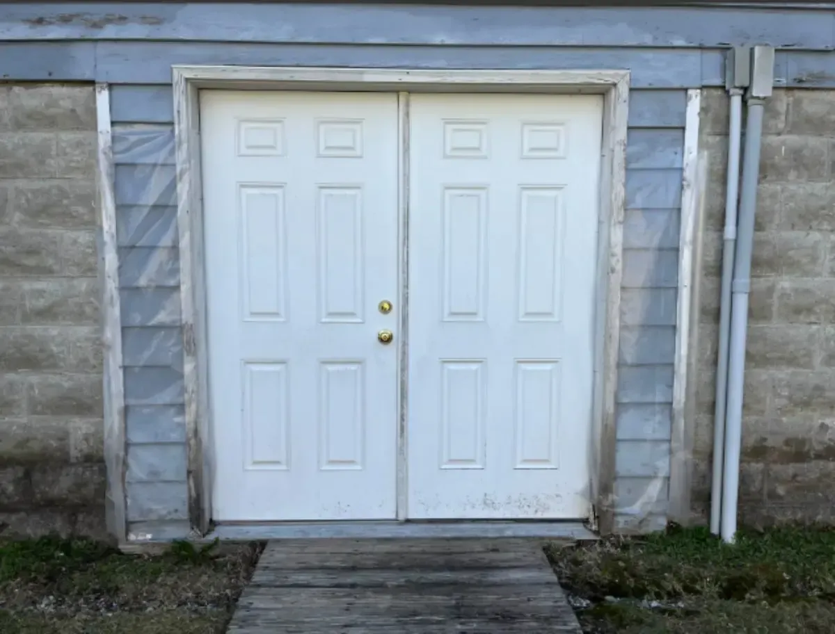 White double doors in a concrete and siding building, with a wooden walkway.