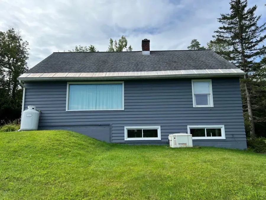 A blue house with a gray roof and white windows is sitting on top of a lush green hill.