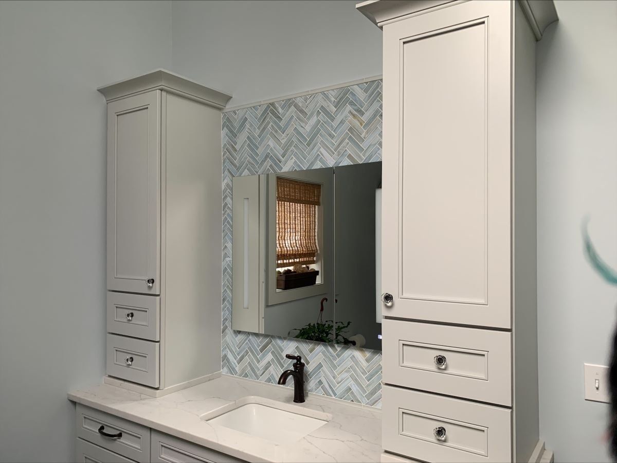 A bathroom with a sink , mirror , cabinets and drawers.