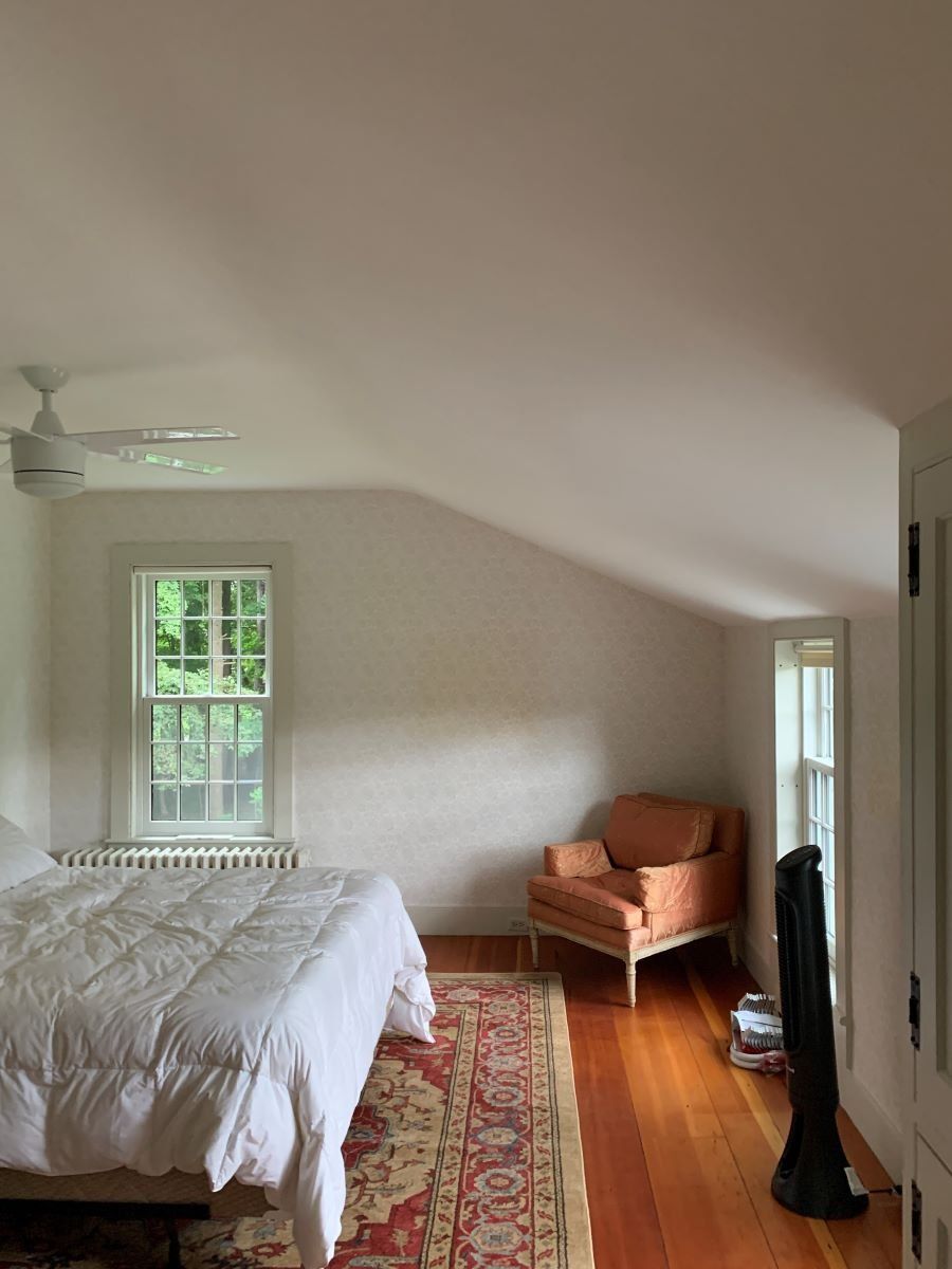 A bedroom with a bed , chair , rug and ceiling fan.