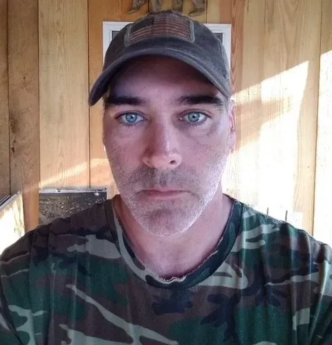 A man is kneeling down on a porch holding a hammer.