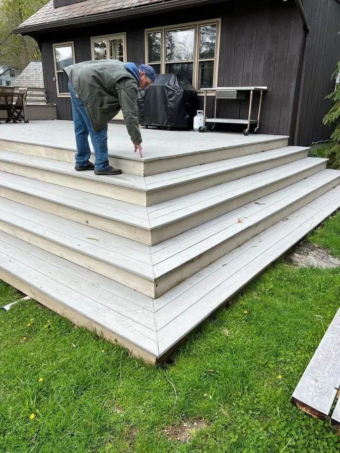 A man is bending over on a deck in front of a house.