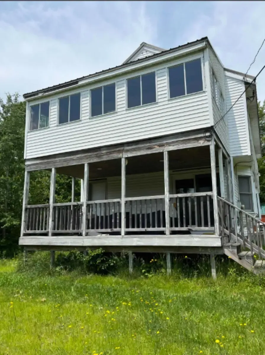 Two-story house with large porch, white siding, tall windows, set in a grassy yard, cloudy sky.