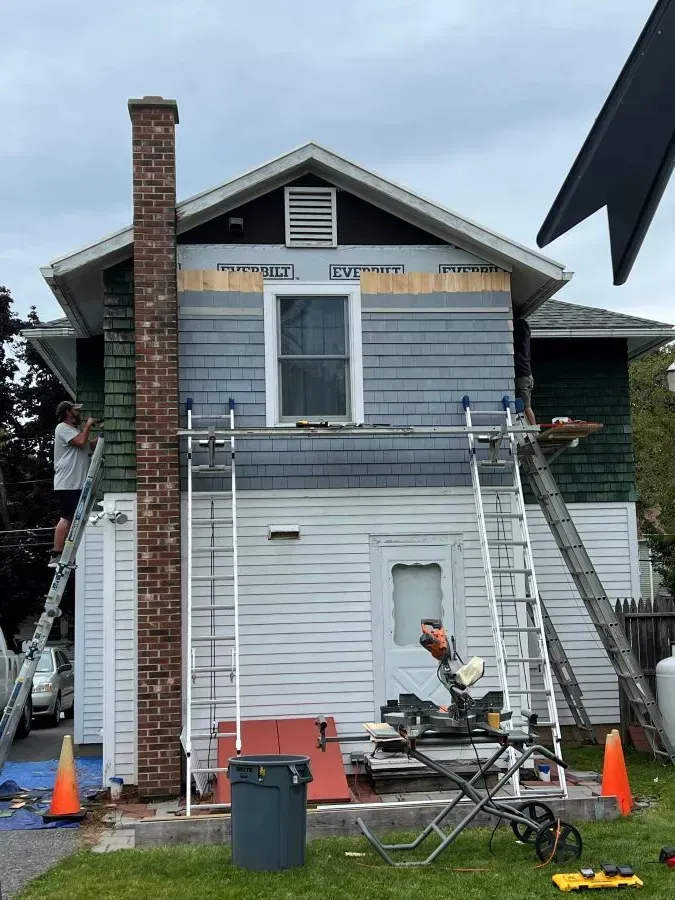 A man is standing on a ladder in front of a house being painted.