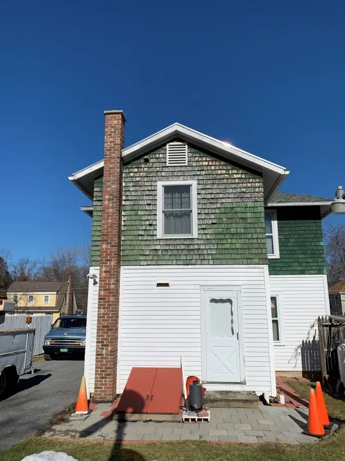 A white house with a green siding and a brick chimney