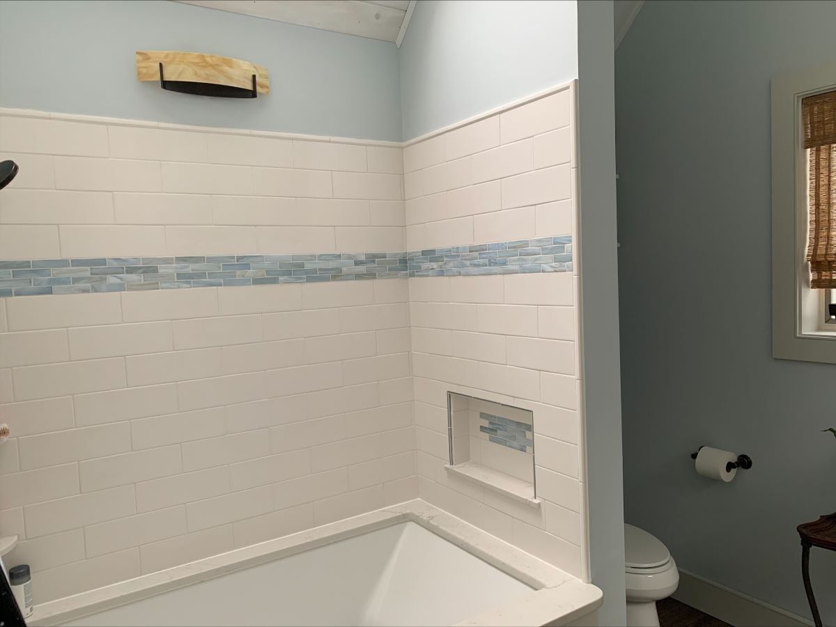 A bathroom with a tub , toilet , shower and window.