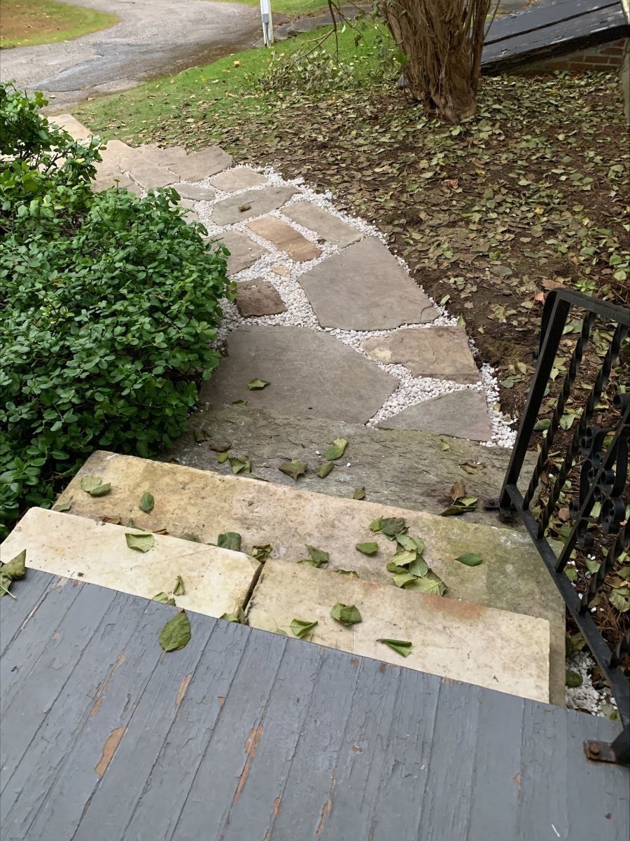 A stone walkway leading up to a deck with leaves on the steps.