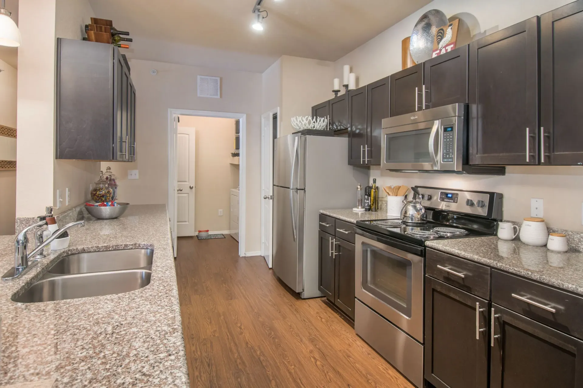 Galley kitchen with dark modern cabinets, granite countertops, stainless-steel appliances, and a double sink.