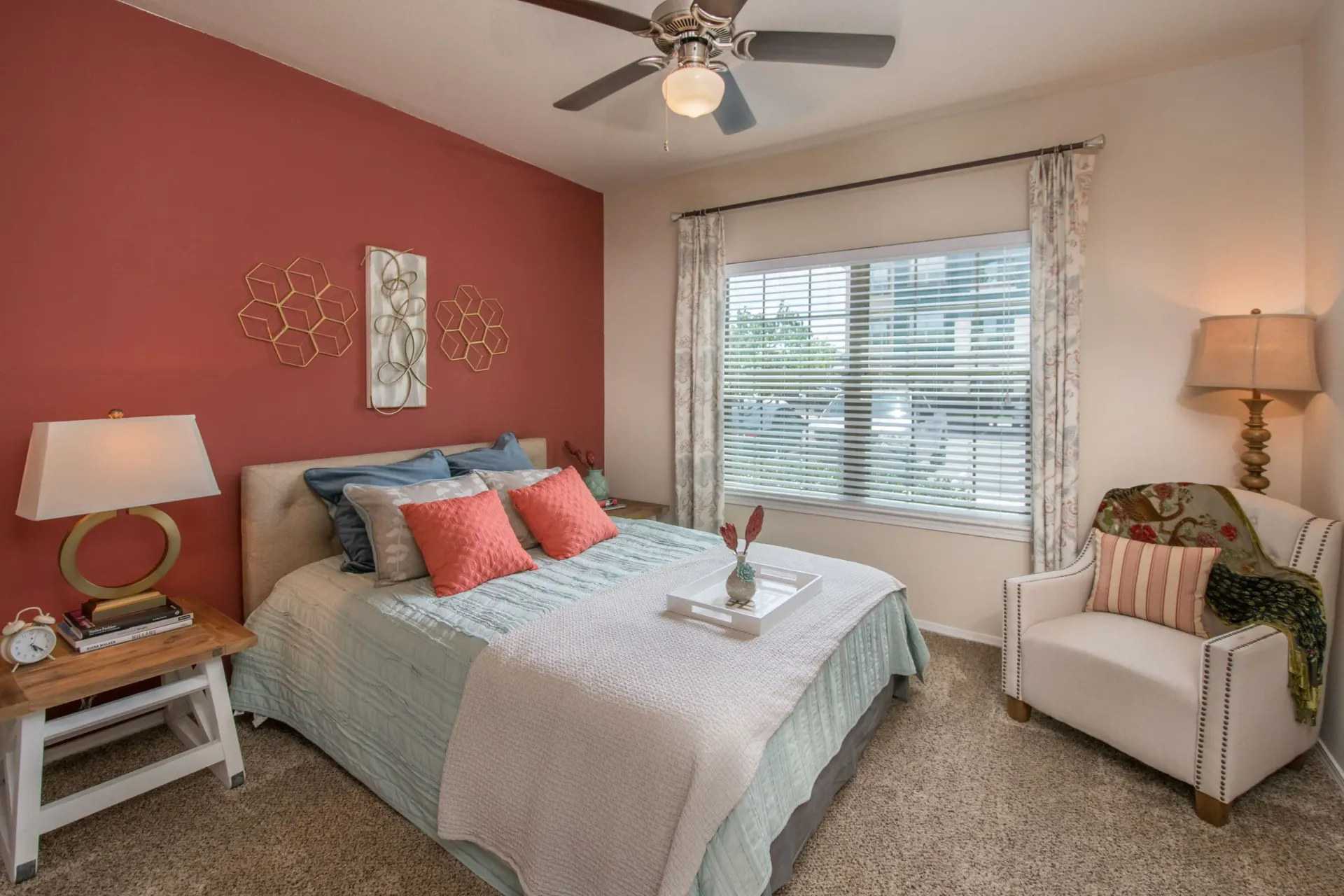 Bedroom in an apartment featuring a bed on a red accent wall, window, and seating area.
