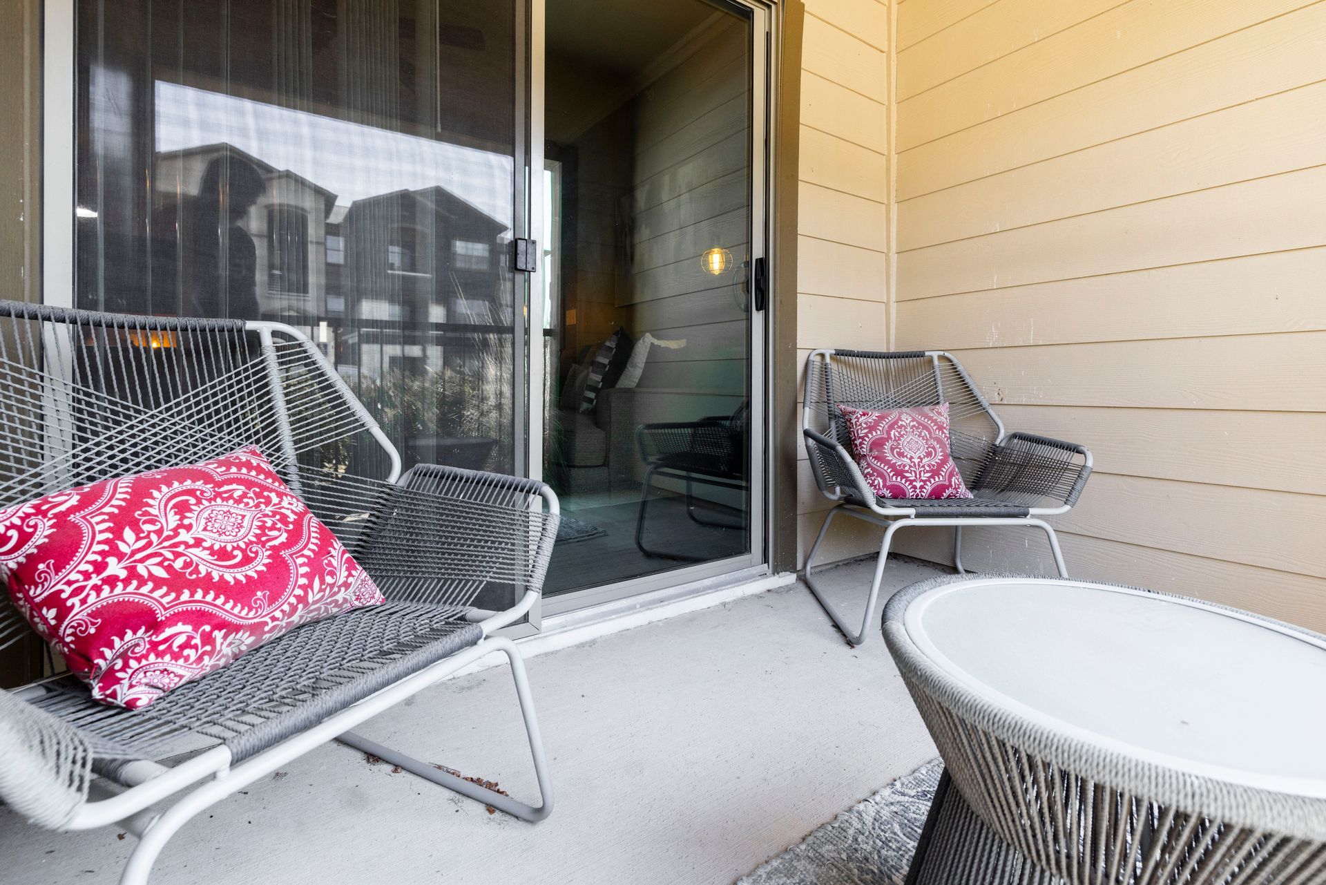 Two modern gray woven patio chairs with pink decorative pillows placed on a balcony next to a small white table.