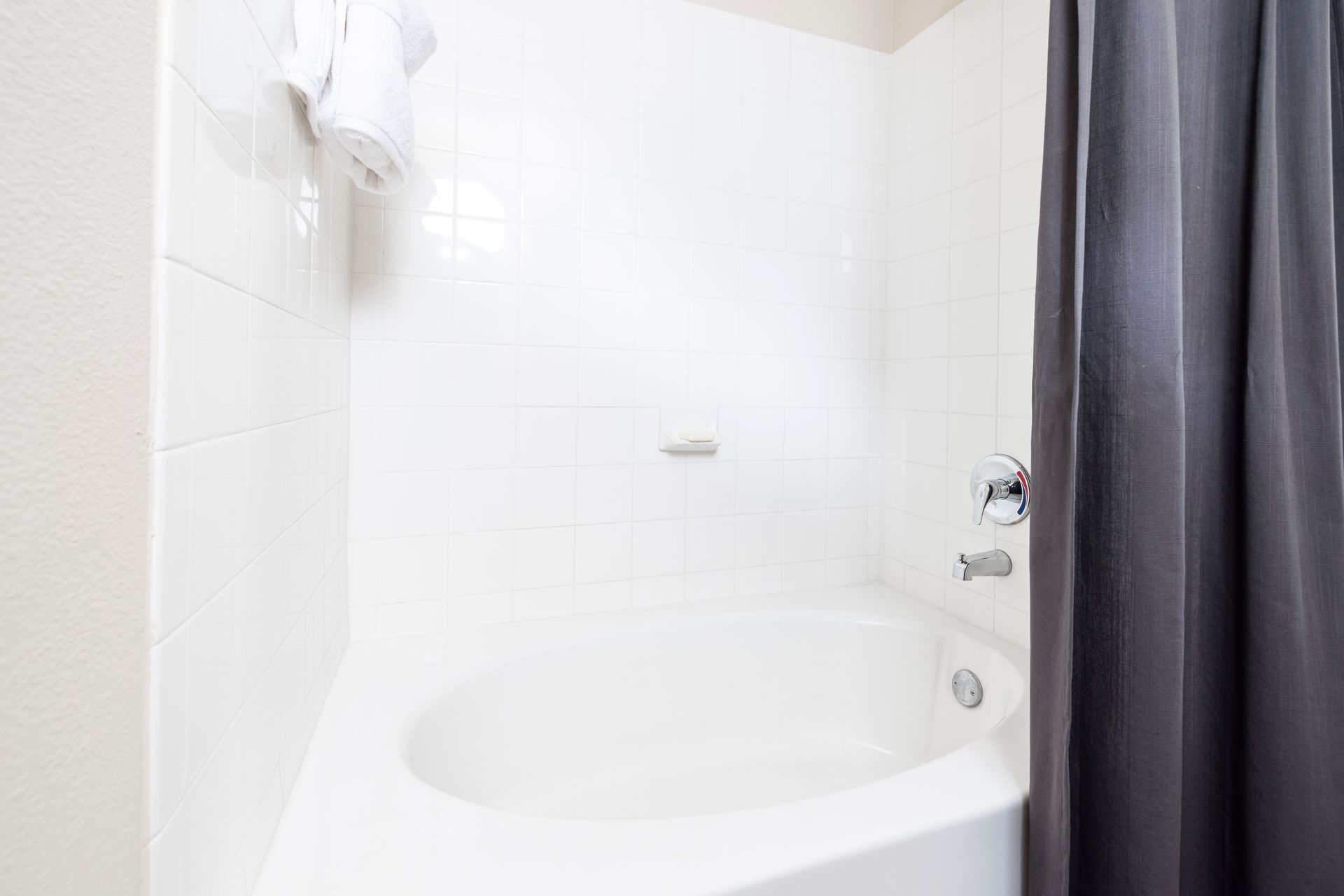 A white bathtub set against tiled walls with a grey shower curtain to the right.
