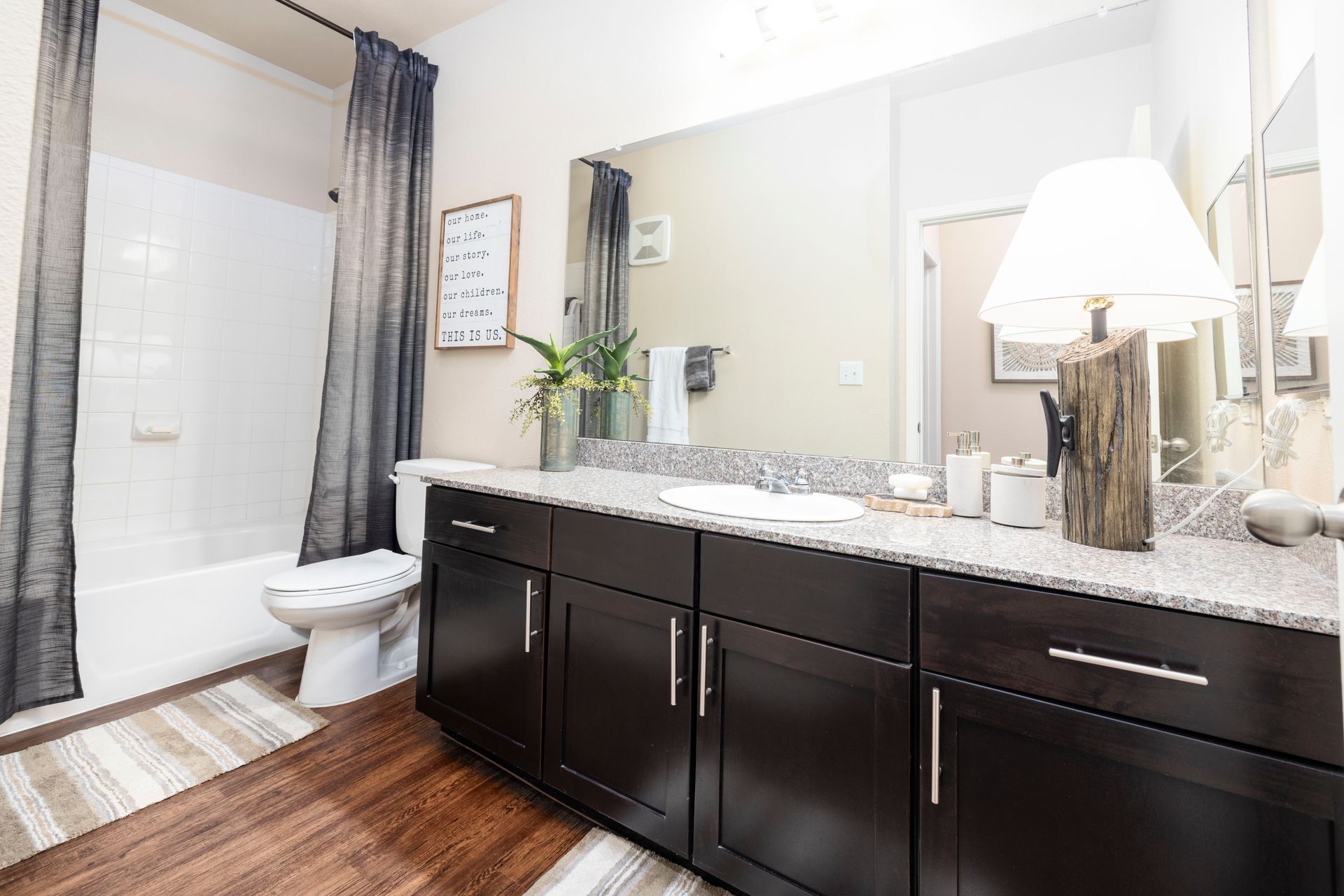 Modern bathroom featuring dark wood cabinets, granite countertops, a large mirror, and a shower with charcoal curtains.