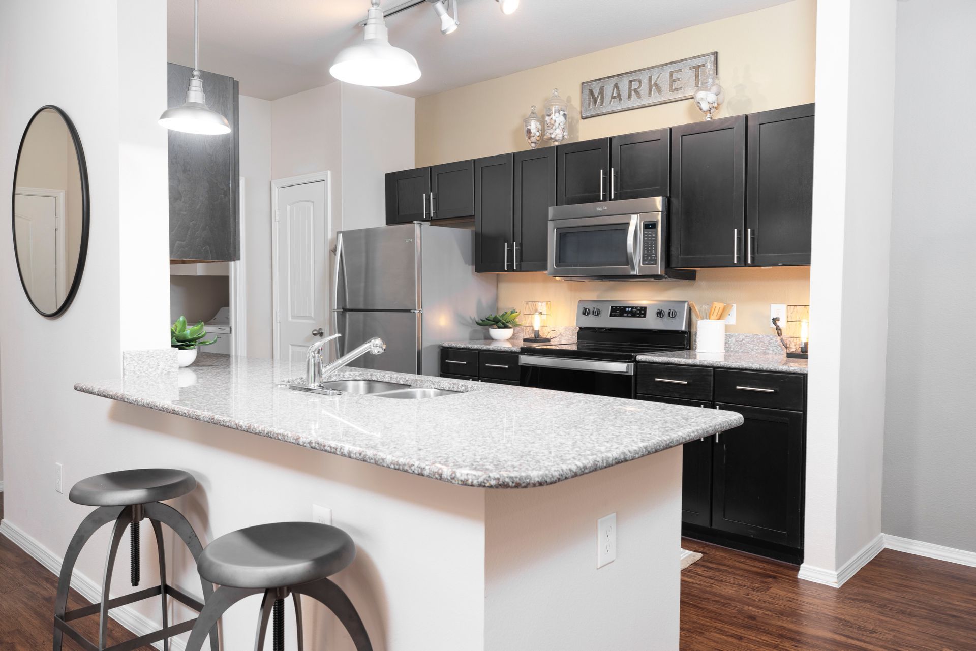 A modern kitchen with black cabinets, stainless steel appliances, a speckled granite island, and two bar stools.