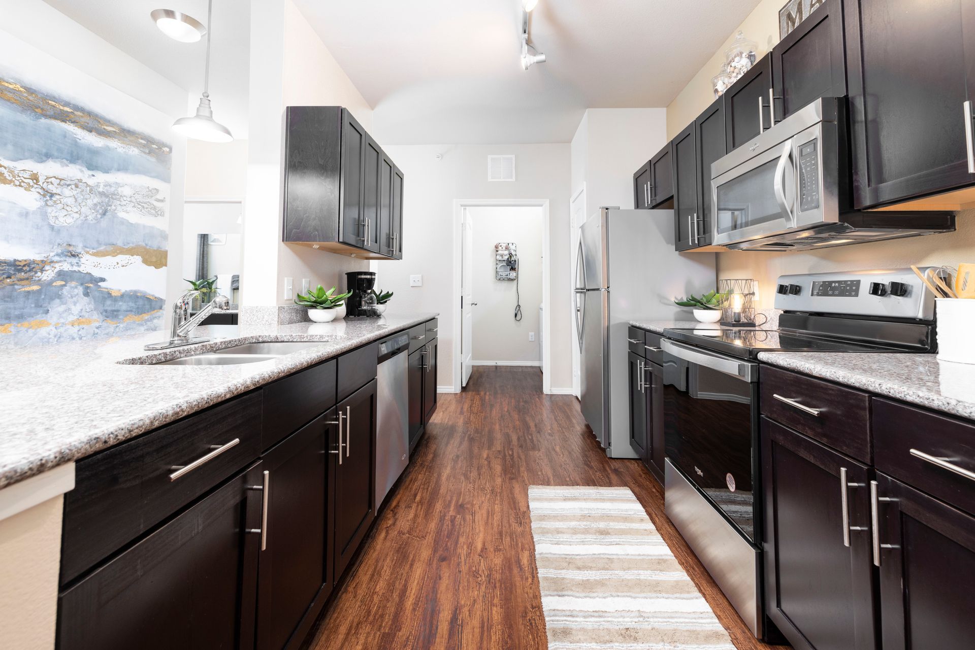 Modern kitchen with dark cabinets, granite countertops, stainless steel appliances, and wood-style flooring.