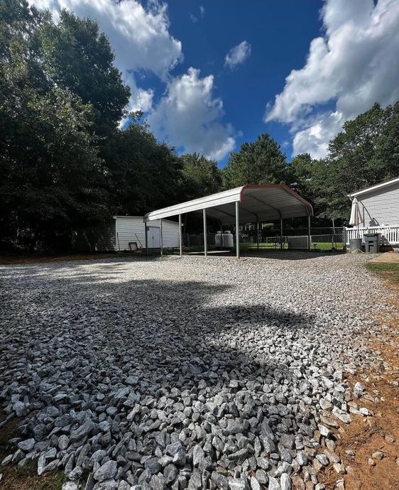 A gravel driveway with a carport in the background