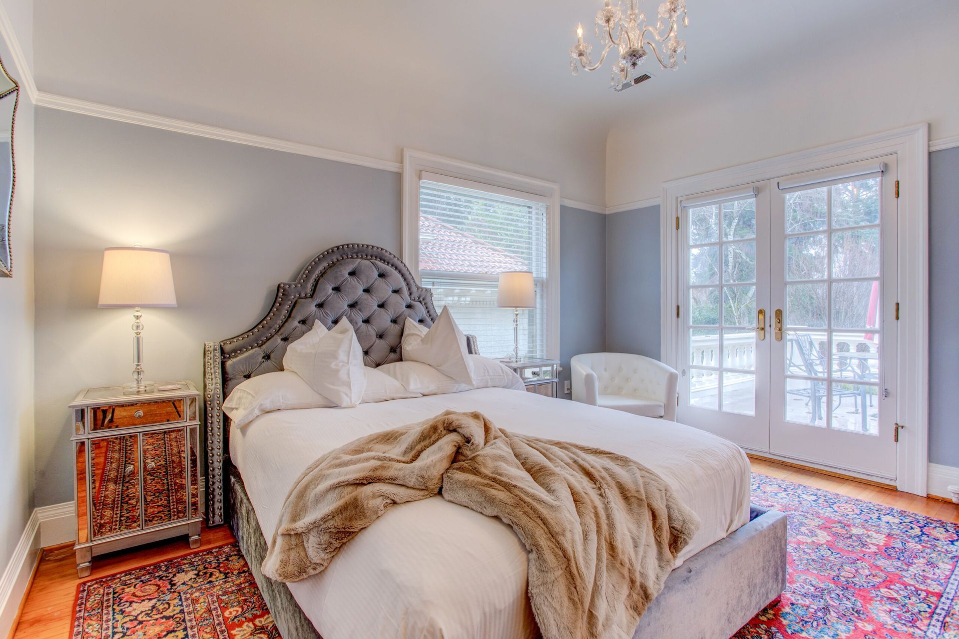 A bedroom with a large bed , two nightstands , a rug and a chandelier.