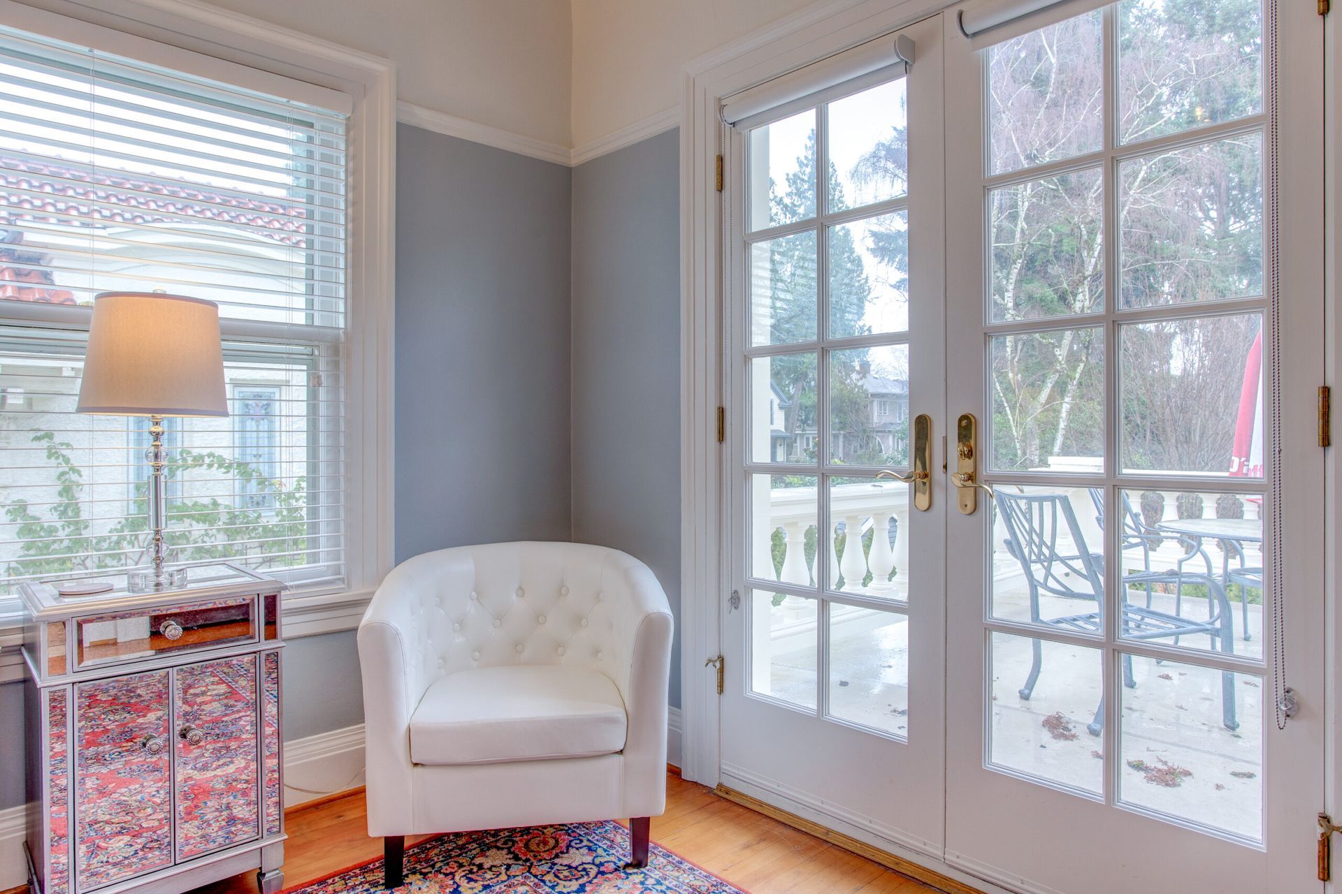 A living room with a white chair and french doors leading to a balcony.