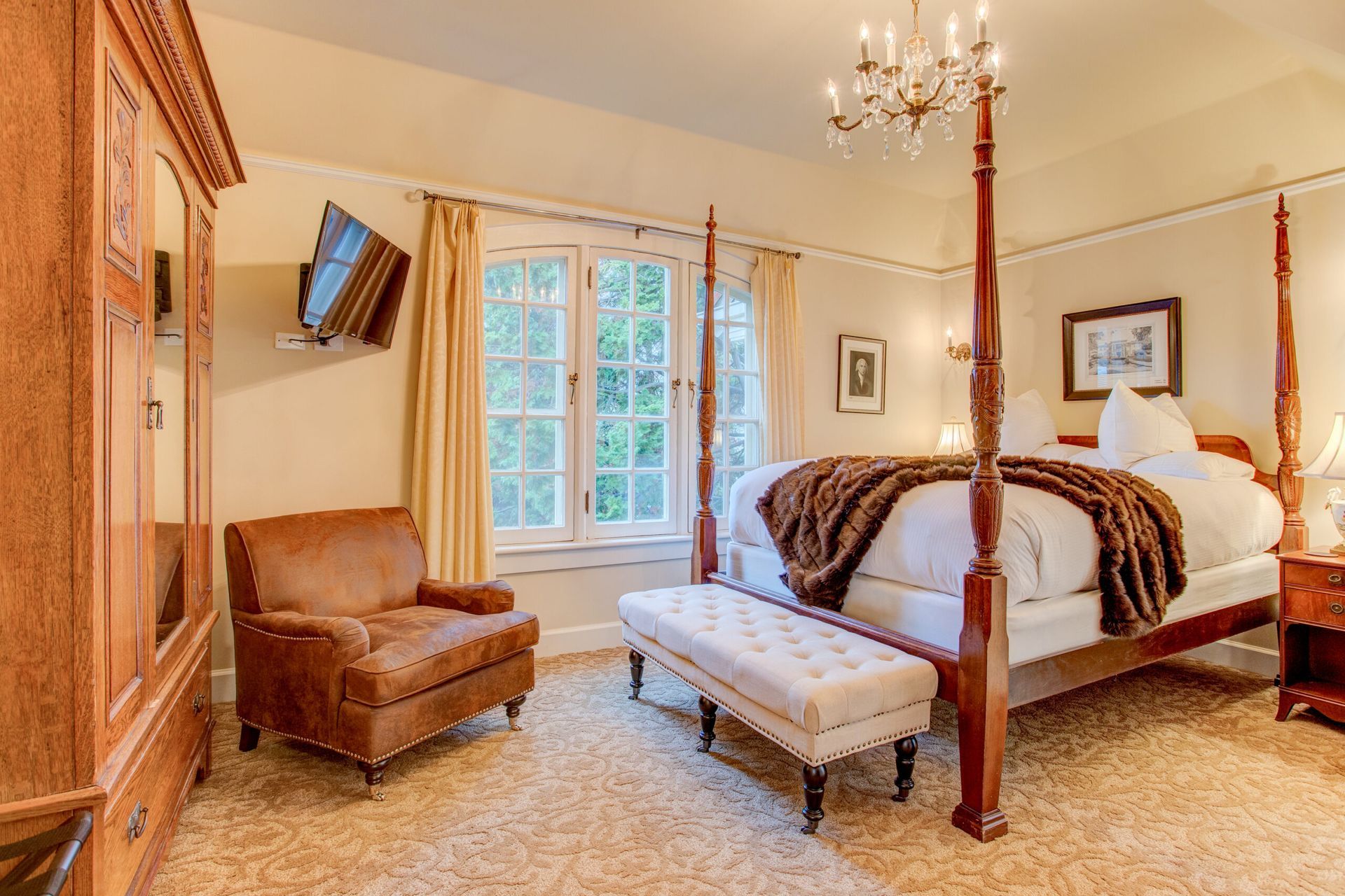 A bedroom with a four poster bed , chair , ottoman and television.