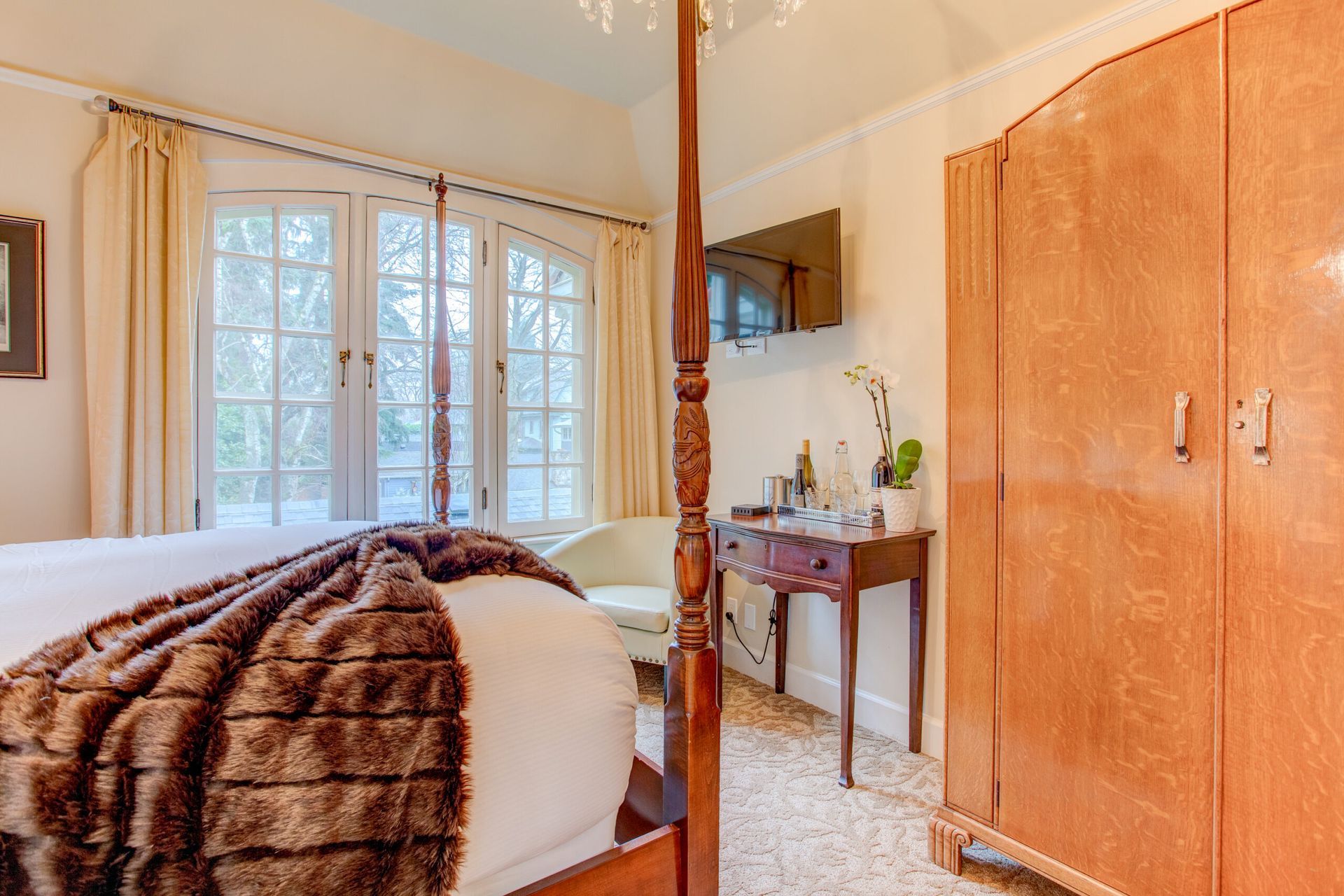 A bedroom with a four poster bed , a desk , a chair and a television.