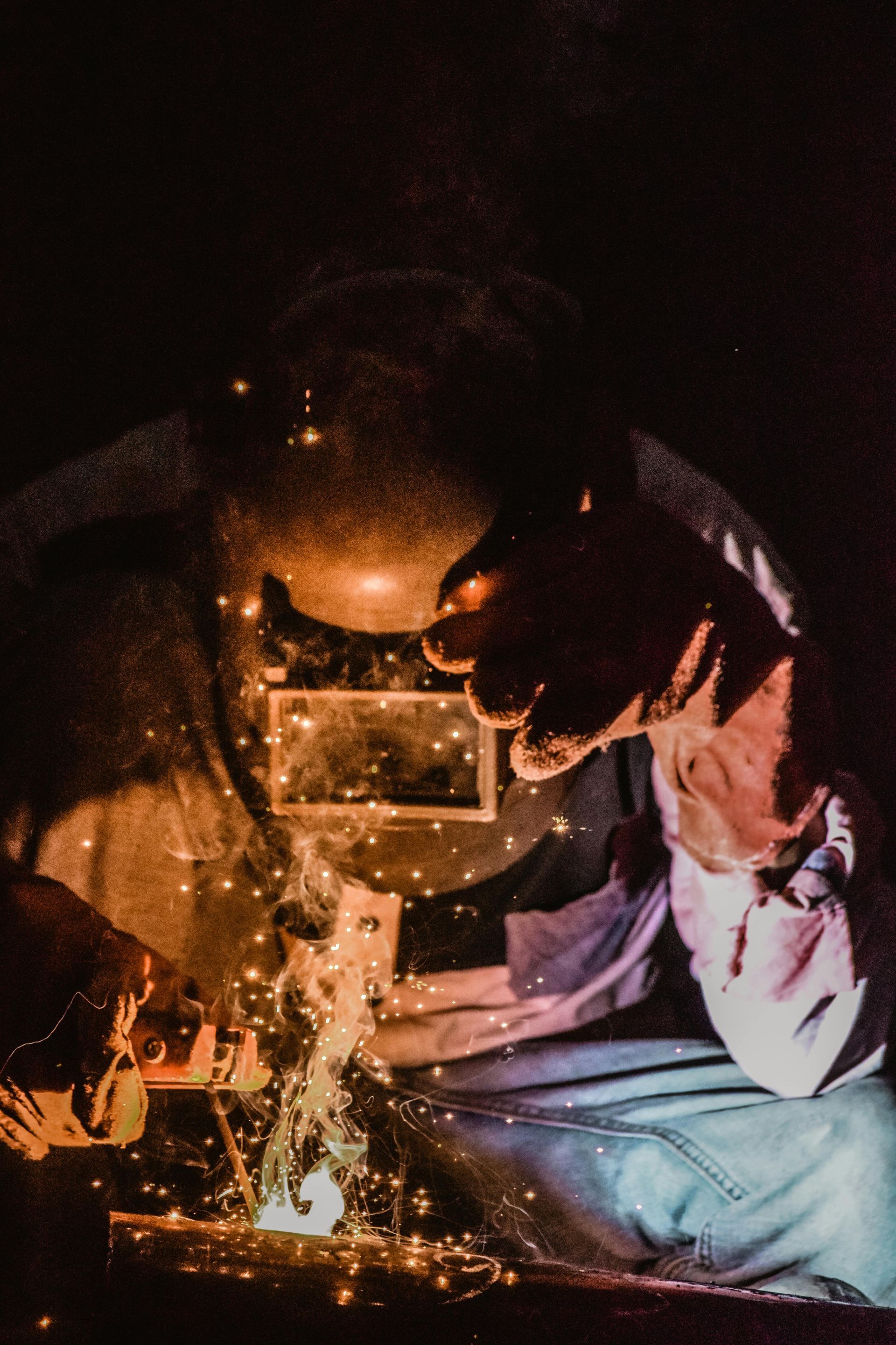 A man is welding a piece of metal in a dark room