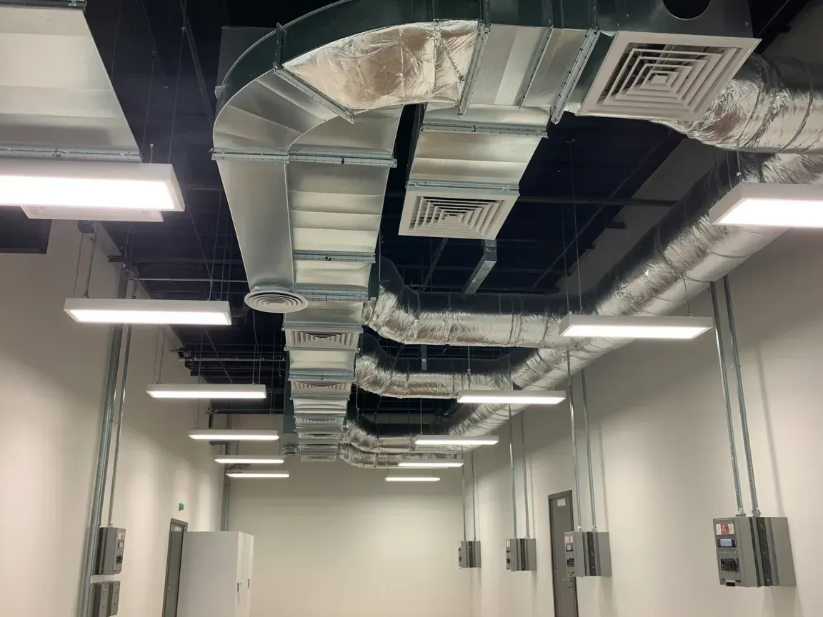 An interior shot of a room with ceiling ductwork, fluorescent lights, and electrical boxes.