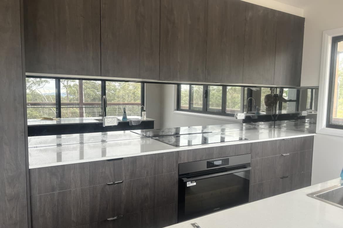 Mirror splashback in modern kitchen reflecting windows, cabinetry and benchtop surfaces clearly