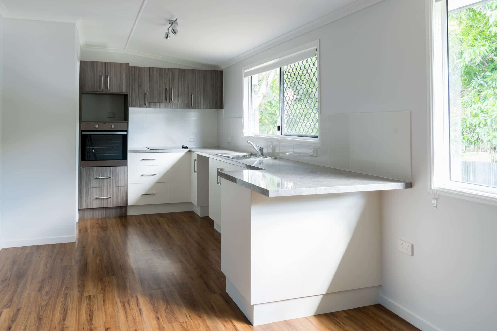 An Empty Kitchen with Wooden Floors and White Cabinets — Colour Splash in Merewether, NSW