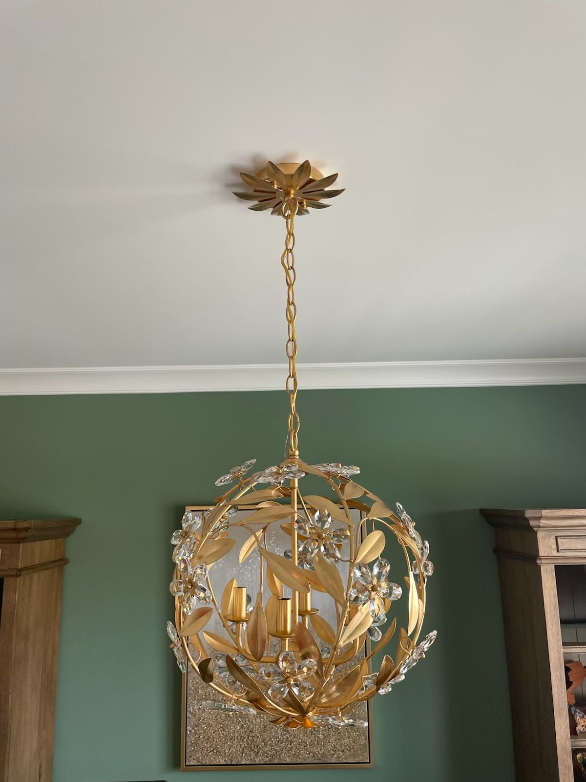 Gold spherical chandelier with crystal accents, hanging from a white ceiling, over green wall.