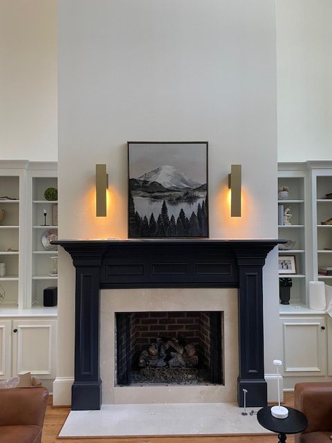 Fireplace with black mantel, flanked by built-in bookshelves. Art and sconces above the hearth.