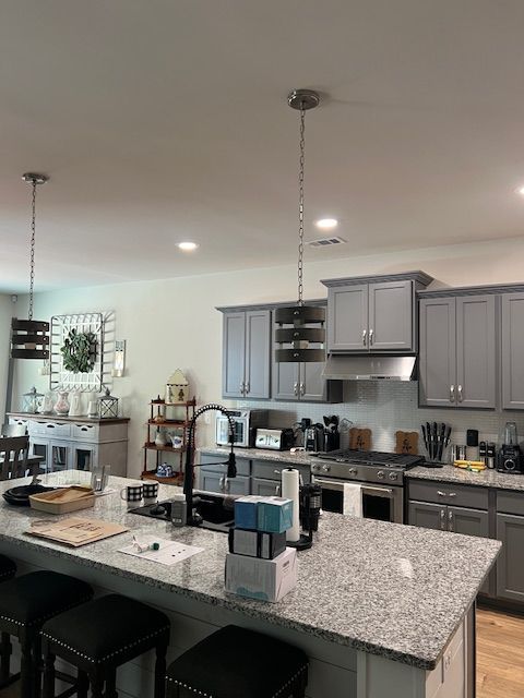 Modern kitchen with gray cabinets, granite countertops, and pendant lights.